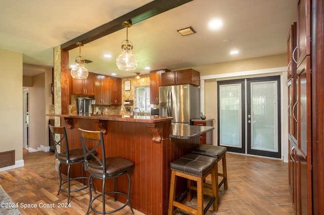 kitchen featuring a breakfast bar area, hanging light fixtures, stainless steel refrigerator with ice dispenser, backsplash, and kitchen peninsula