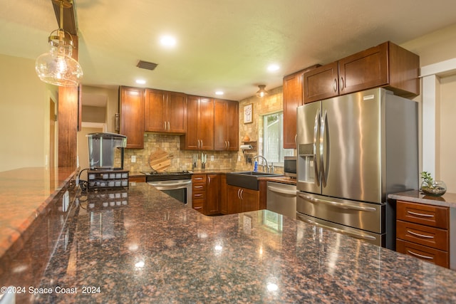 kitchen with tasteful backsplash, sink, stainless steel appliances, dark stone counters, and decorative light fixtures