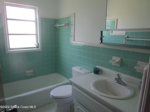 full bathroom with tile patterned floors, toilet, tiled shower / bath, vanity, and tile walls