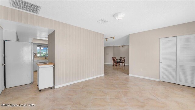 interior space featuring a textured ceiling, light tile patterned flooring, and white fridge