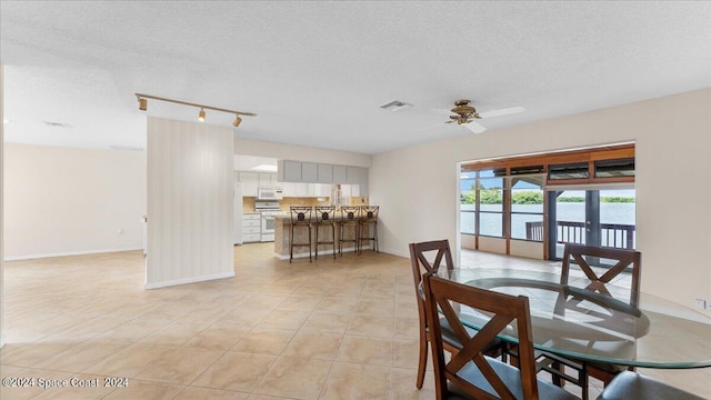 tiled dining space featuring a textured ceiling, track lighting, a water view, ceiling fan, and french doors