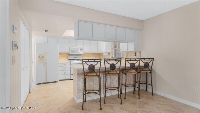 kitchen with a kitchen breakfast bar, decorative backsplash, white cabinetry, white appliances, and kitchen peninsula