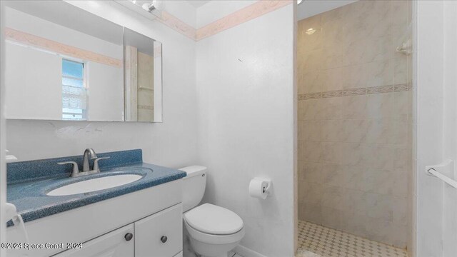 bathroom featuring a tile shower, vanity, and toilet