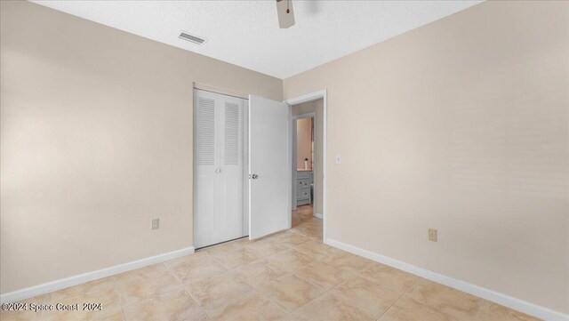 unfurnished bedroom with a textured ceiling, light tile patterned floors, ceiling fan, and a closet