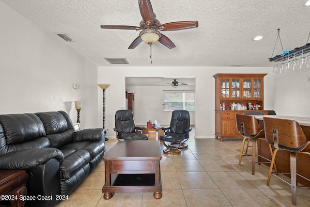 living room featuring a textured ceiling, ceiling fan, light tile patterned flooring, and bar