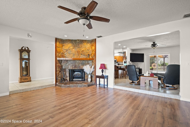 living room featuring ceiling fan, a textured ceiling, light hardwood / wood-style flooring, and a fireplace