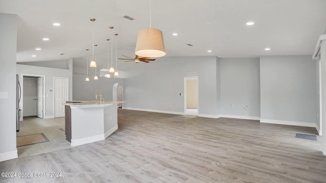 kitchen with hanging light fixtures, light stone countertops, light hardwood / wood-style floors, sink, and high vaulted ceiling