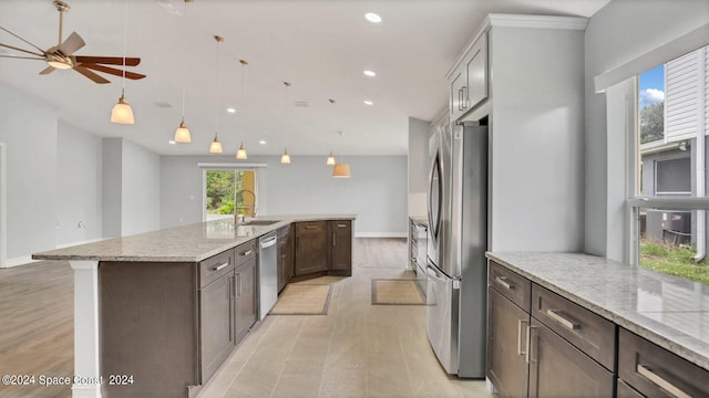 kitchen with light stone counters, sink, ceiling fan, appliances with stainless steel finishes, and a center island with sink