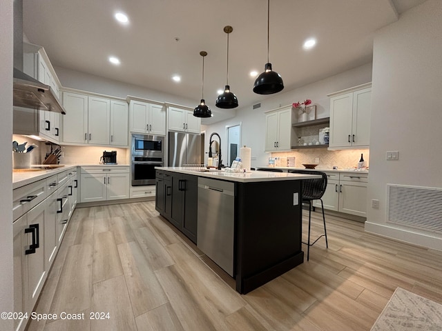 kitchen featuring light hardwood / wood-style flooring, appliances with stainless steel finishes, white cabinets, and a kitchen island with sink