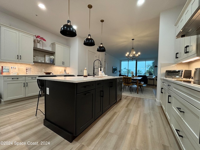 kitchen featuring a kitchen island with sink, an inviting chandelier, decorative light fixtures, and white cabinets