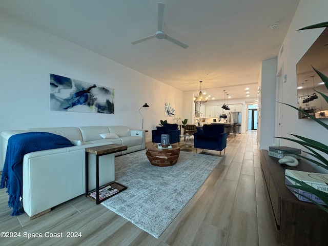 living room featuring ceiling fan with notable chandelier and light hardwood / wood-style floors