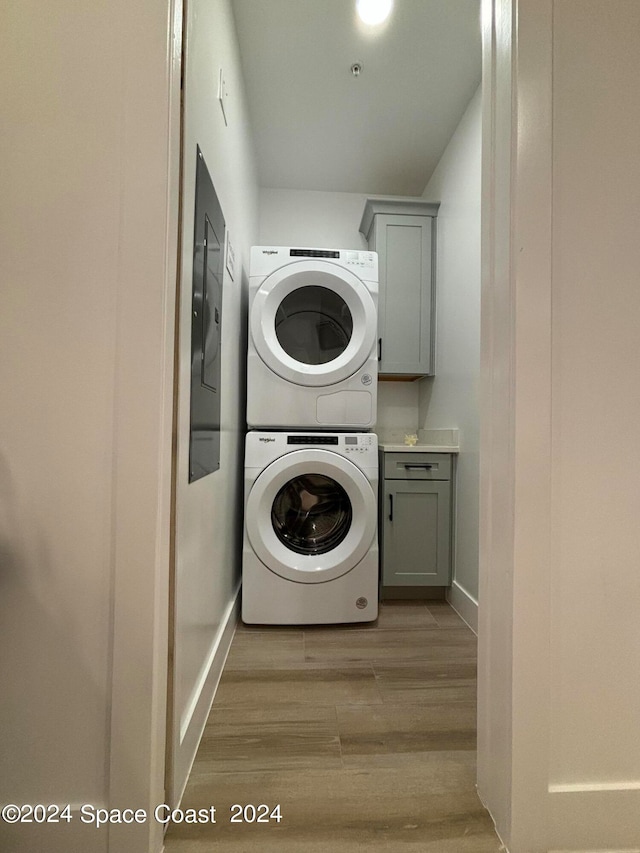 clothes washing area featuring light hardwood / wood-style flooring, cabinets, and stacked washer / drying machine