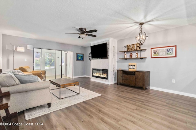 living room featuring a textured ceiling, a fireplace, hardwood / wood-style floors, and ceiling fan with notable chandelier