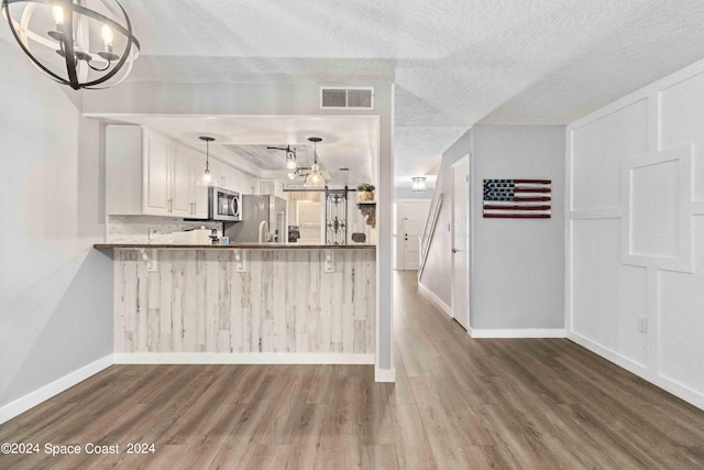 kitchen with white cabinetry, kitchen peninsula, wood-type flooring, a textured ceiling, and appliances with stainless steel finishes