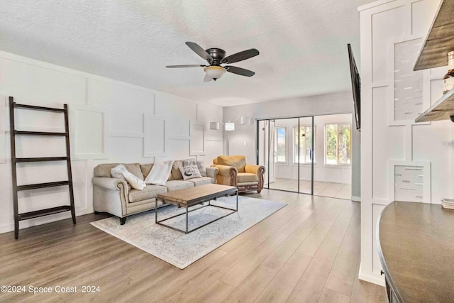 living room featuring a textured ceiling, light hardwood / wood-style flooring, and ceiling fan