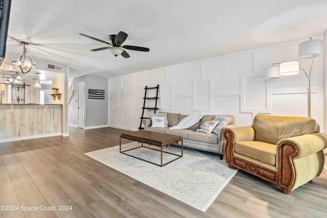 living room featuring ceiling fan with notable chandelier, wood-type flooring, and a textured ceiling