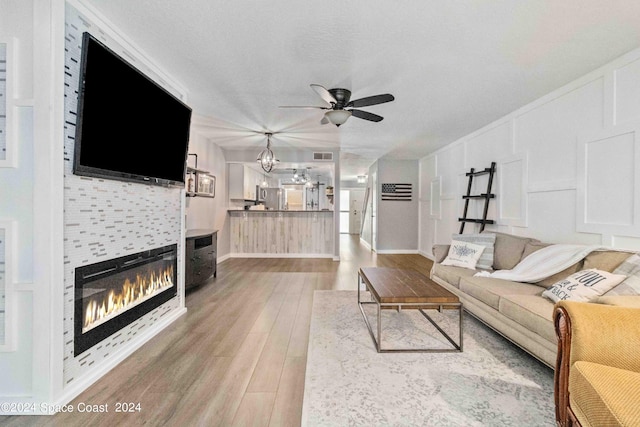 living room with a textured ceiling, a fireplace, ceiling fan with notable chandelier, and hardwood / wood-style flooring