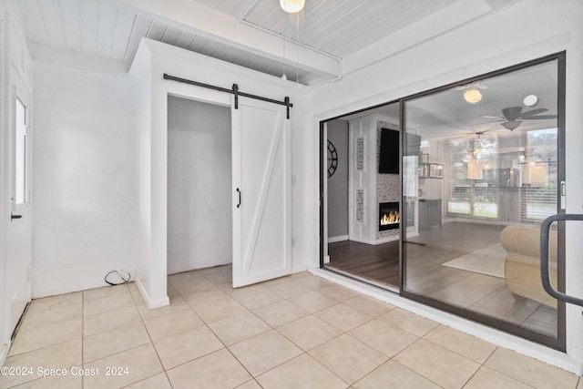 tiled spare room with wood ceiling, a large fireplace, ceiling fan, a barn door, and beamed ceiling