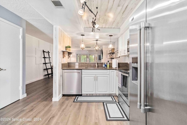 kitchen with white cabinets, decorative light fixtures, stainless steel appliances, and light hardwood / wood-style flooring