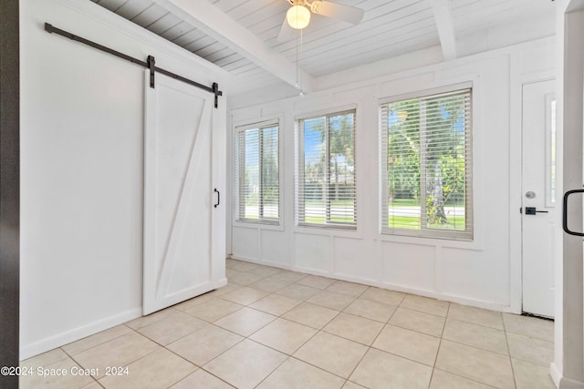 interior space with a barn door, ceiling fan, beamed ceiling, and multiple windows