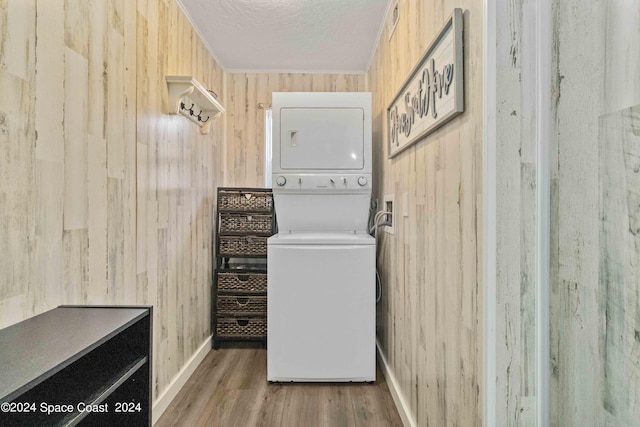 laundry area with wooden walls, stacked washing maching and dryer, and wood-type flooring