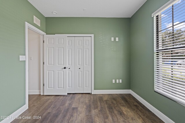 unfurnished bedroom featuring multiple windows, dark hardwood / wood-style floors, and a closet