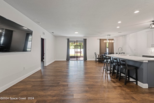 kitchen featuring a textured ceiling, a breakfast bar area, dark hardwood / wood-style floors, decorative light fixtures, and a kitchen island with sink