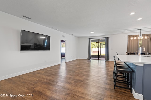 unfurnished living room featuring a textured ceiling, dark wood-type flooring, sink, and a chandelier