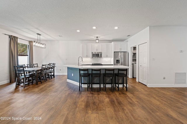 kitchen featuring a kitchen island with sink, white cabinetry, decorative light fixtures, dark hardwood / wood-style flooring, and appliances with stainless steel finishes