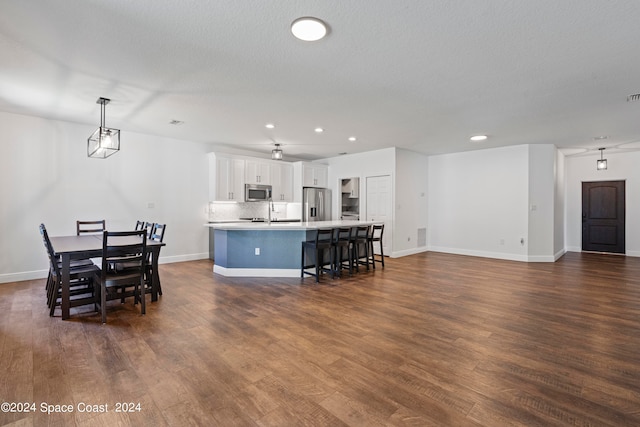 kitchen featuring dark hardwood / wood-style floors, a center island with sink, a breakfast bar, stainless steel appliances, and white cabinets