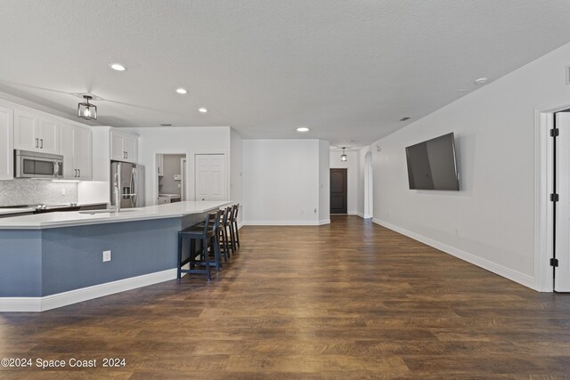 kitchen with appliances with stainless steel finishes, white cabinetry, an island with sink, dark wood-type flooring, and a kitchen bar