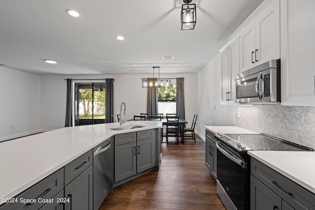 kitchen with hanging light fixtures, stainless steel appliances, white cabinetry, sink, and dark hardwood / wood-style floors