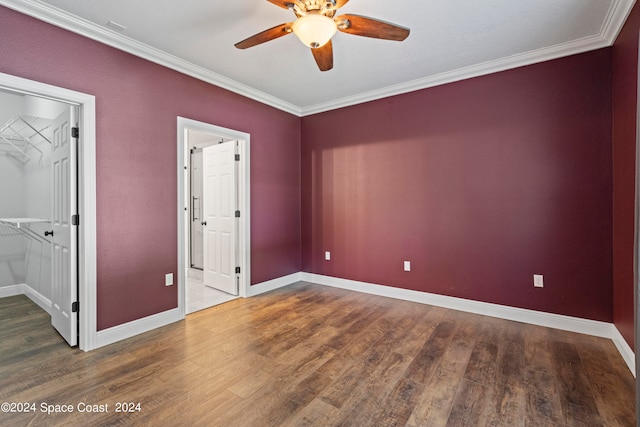 unfurnished bedroom featuring a walk in closet, a closet, crown molding, dark wood-type flooring, and ceiling fan