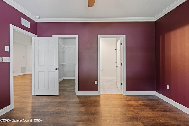 unfurnished bedroom featuring ornamental molding, dark hardwood / wood-style flooring, a walk in closet, and ceiling fan