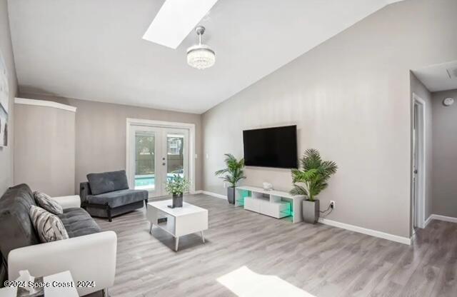 living room featuring a skylight, high vaulted ceiling, and light hardwood / wood-style floors