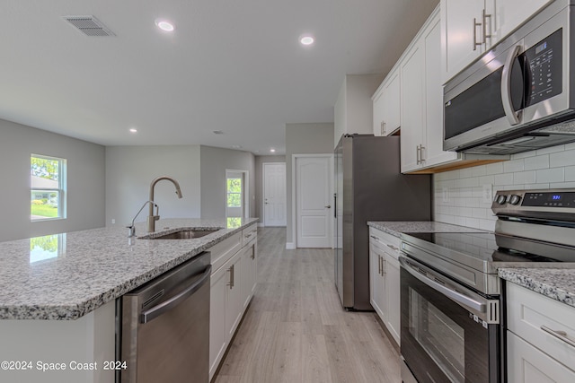 kitchen with stainless steel appliances, an island with sink, sink, white cabinets, and light hardwood / wood-style floors