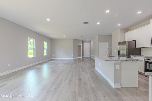 kitchen with light wood-type flooring, white cabinetry, stainless steel appliances, light stone counters, and a center island with sink