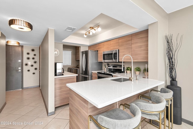 kitchen featuring stainless steel appliances, kitchen peninsula, sink, a breakfast bar, and light tile patterned flooring