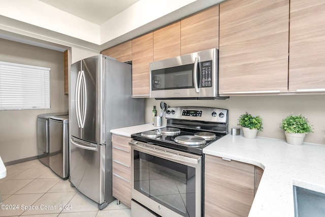 kitchen featuring appliances with stainless steel finishes, light tile patterned floors, light stone countertops, and washer and dryer