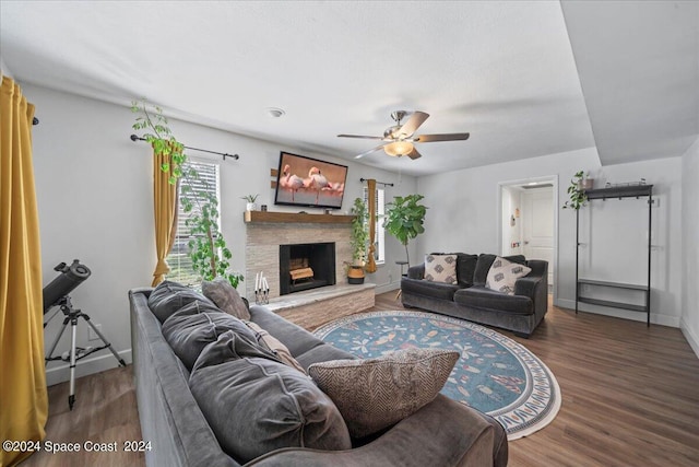 living room with dark wood-type flooring, ceiling fan, and a stone fireplace