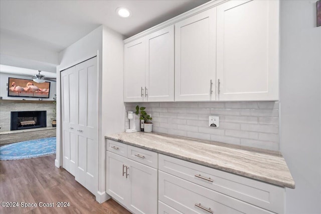 kitchen with white cabinets, ceiling fan, light stone counters, and light hardwood / wood-style flooring