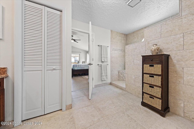 bathroom featuring tile patterned flooring, a textured ceiling, ceiling fan, vaulted ceiling, and tile walls