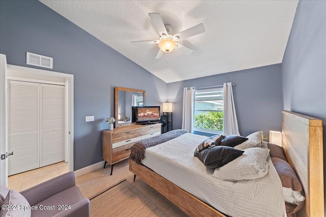 bedroom with vaulted ceiling, a closet, light tile patterned flooring, ceiling fan, and a textured ceiling