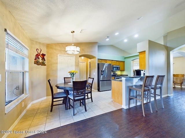 dining area with a textured ceiling, light hardwood / wood-style floors, and lofted ceiling