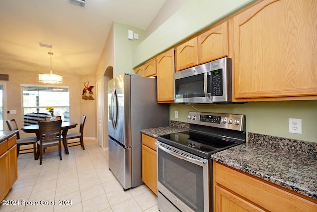 kitchen featuring light tile patterned flooring, vaulted ceiling, stainless steel appliances, an inviting chandelier, and dark stone counters