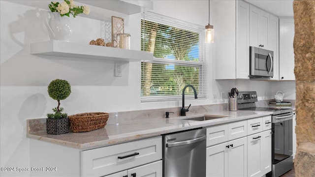 kitchen featuring white cabinetry, stainless steel appliances, light stone counters, sink, and hanging light fixtures