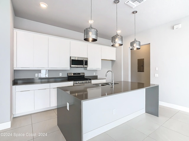 kitchen with a kitchen island with sink, pendant lighting, stainless steel appliances, sink, and white cabinets