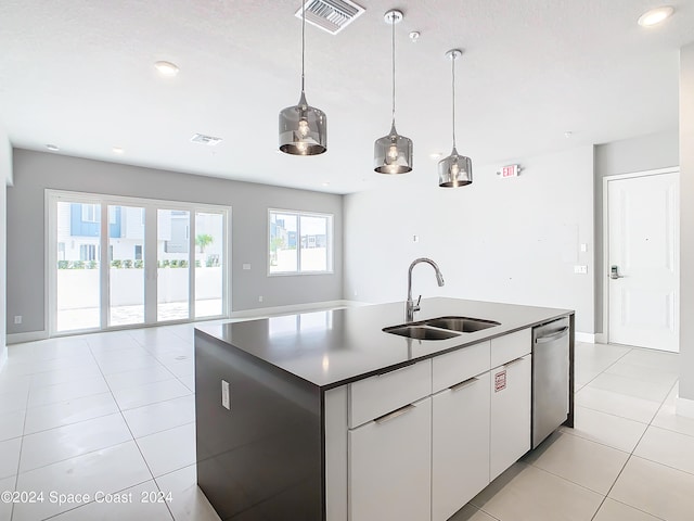 kitchen featuring a kitchen island with sink, light tile patterned floors, sink, stainless steel dishwasher, and white cabinets