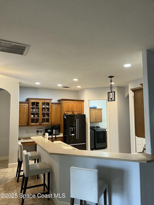 kitchen with a breakfast bar, kitchen peninsula, washing machine and clothes dryer, and high end black fridge