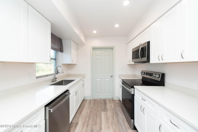 kitchen with appliances with stainless steel finishes, sink, light wood-type flooring, and white cabinets